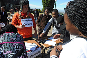 Taking action: Roscoe Jacobs, wearing orange, holds up a placard demanding the return of school girls that were kidnapped in Nigeria in April, while students sign a petition urging the South African government to step in.