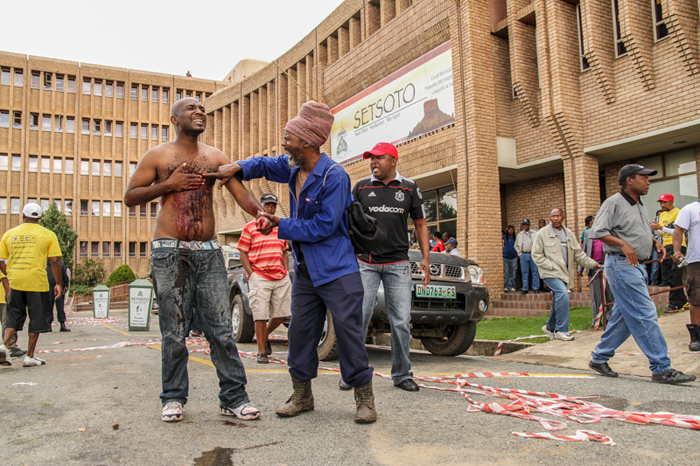 Andries Tatane – who joined some 4 000 Ficksburg residents on 13 April 2011 to protest poor service delivery in the area – clutches his chest after police shot him with rubber bullets; he collapsed and died 20 minutes later.