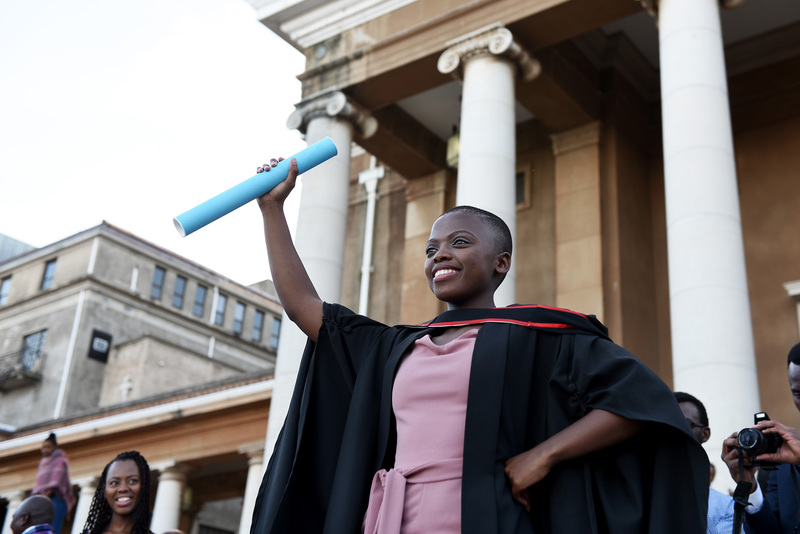 A UCT graduate poses outside Memorial Hall after receiving their degree.