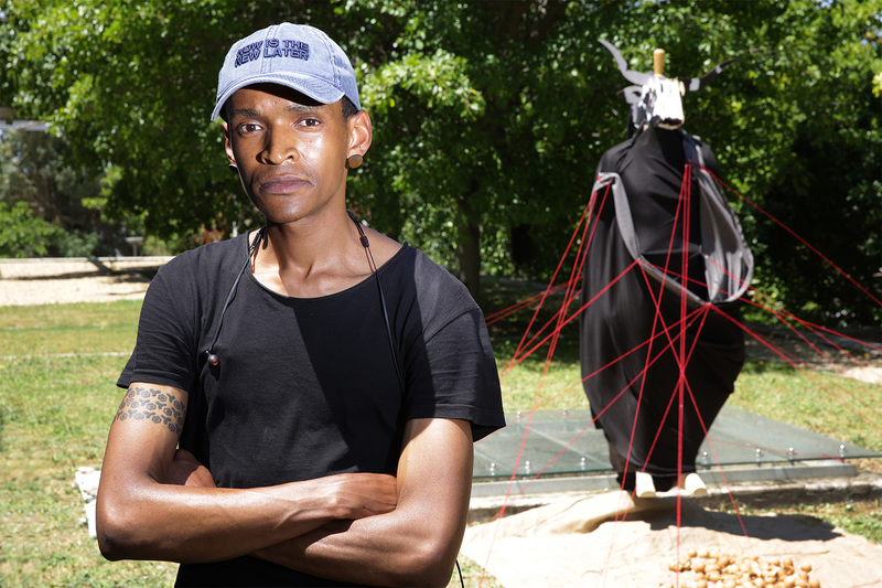 Final-year law student Kneo Mokgopa with the installation, which comprises a mannequin draped in black fabric with a cardboard bull’s head, tethered to the ground with a network of red ropes and approached via a path strewn with eggshells.