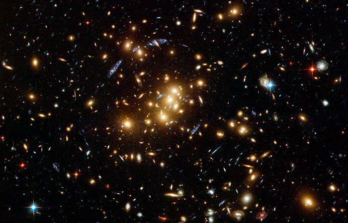 This rich galaxy cluster, catalogued as CL0024+17, is allowing astronomers to probe the distribution of dark matter in space. The blue streaks near the centre of the image are the smeared images of very distant galaxies that are not part of the cluster. The distant galaxies appear distorted because their light is being bent and magnified by the powerful gravity of CL0024+17, an effect called gravitational lensing. Dark matter cannot be seen because it does not shine or reflect light. Astronomers can only detect its influence by how its gravity affects light. By mapping the distorted light created by gravitational lensing, astronomers can trace how dark matter is distributed in the cluster. The Hubble observations were taken in November 2004 by the Advanced Camera for Surveys, and accessed via <a href="http://commons.wikimedia.org/wiki/File:CL0024%2B17opt.jpg" target="_blank">Wikimedia Commons</a>.