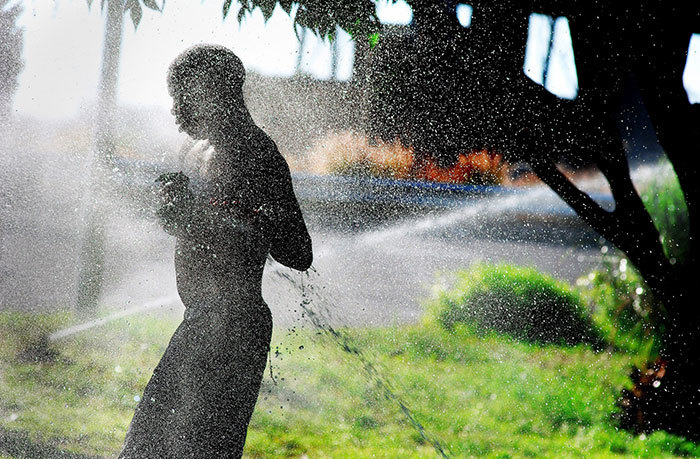A homeless man washes himself using a sprinkler.