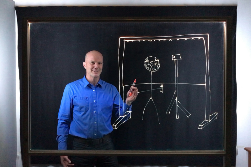 Assoc Prof Jimmy Winfield demonstrating the lightboard setup, revealing the wooden frame and dropcloth behind him.