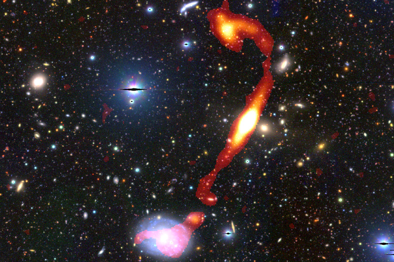 The newly discovered giant radio galaxy ‘Inkathazo’. The glowing plasma jets, as seen by the MeerKAT telescope, are shown in red and yellow. The starlight from other surrounding galaxies can be seen in the background.