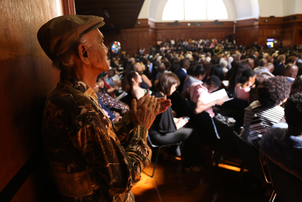 A proud grandparent claps in acknowledgement as his grandchild graduates.