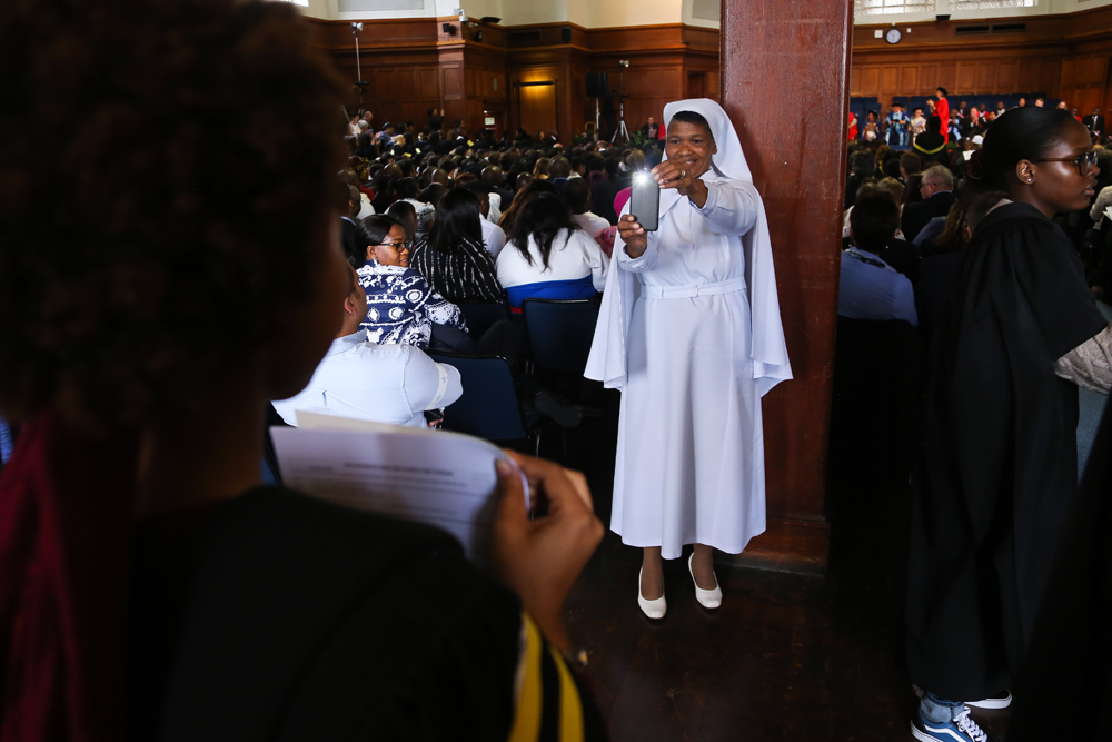 A proud mother photographs her daughter with her degree certificate.