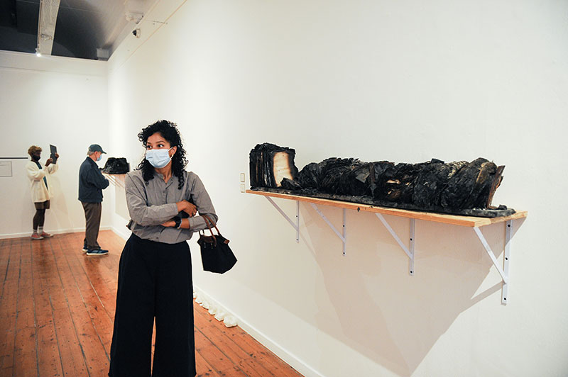 Charred wooden book rack and unidentifiable contents provide a stark backdrop 